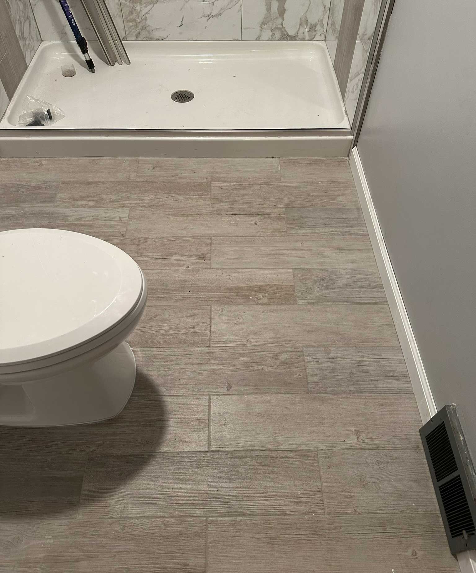 Bathroom with toilet, shower, and wood-look floor tiles. A small vent is visible.