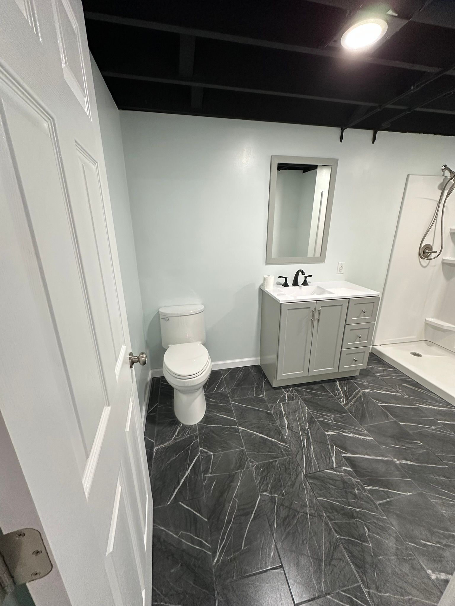 Bathroom with a toilet, vanity, and shower. Black flooring, light blue walls, and a black ceiling.
