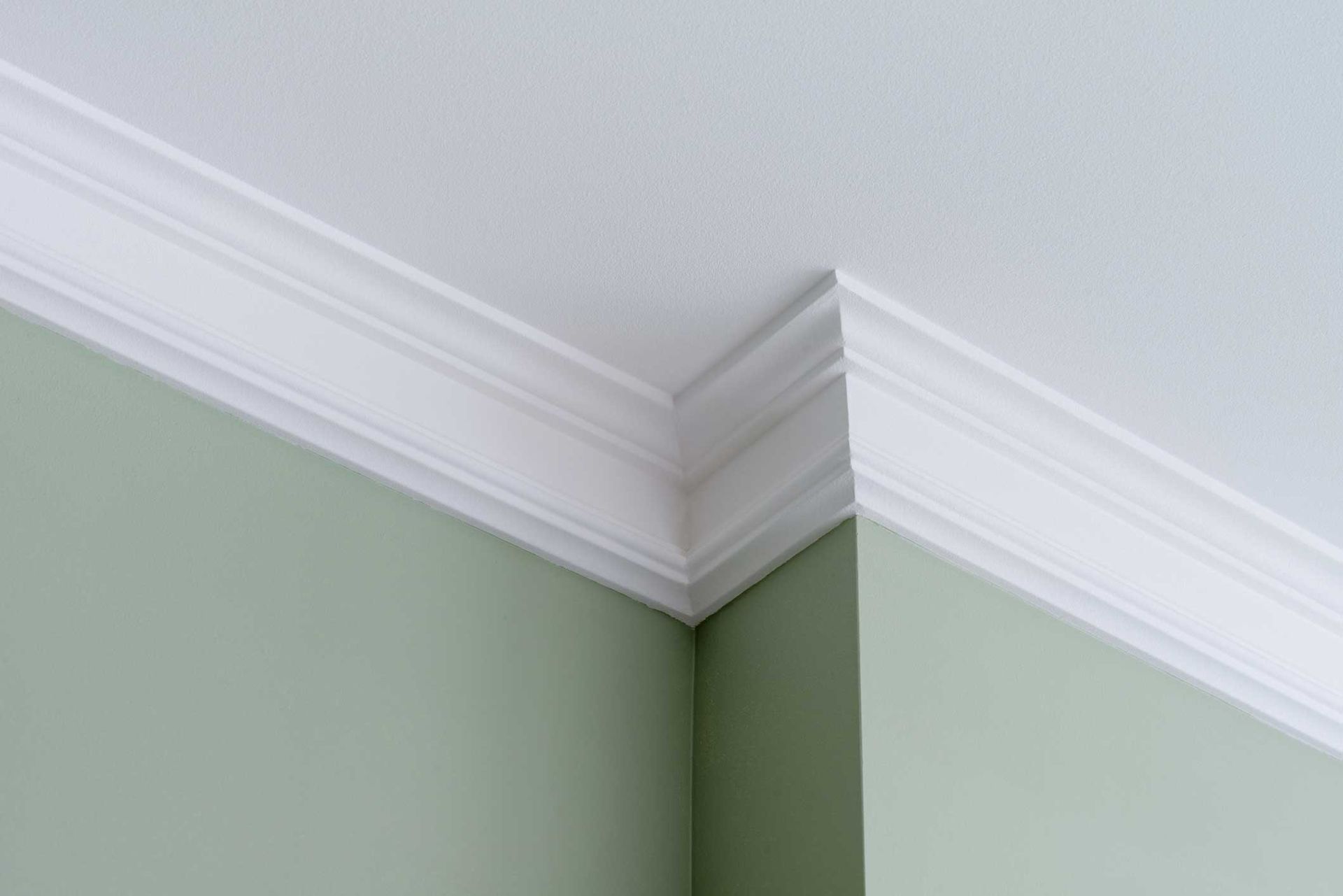 White crown molding at the corner of a light green painted room and white ceiling.