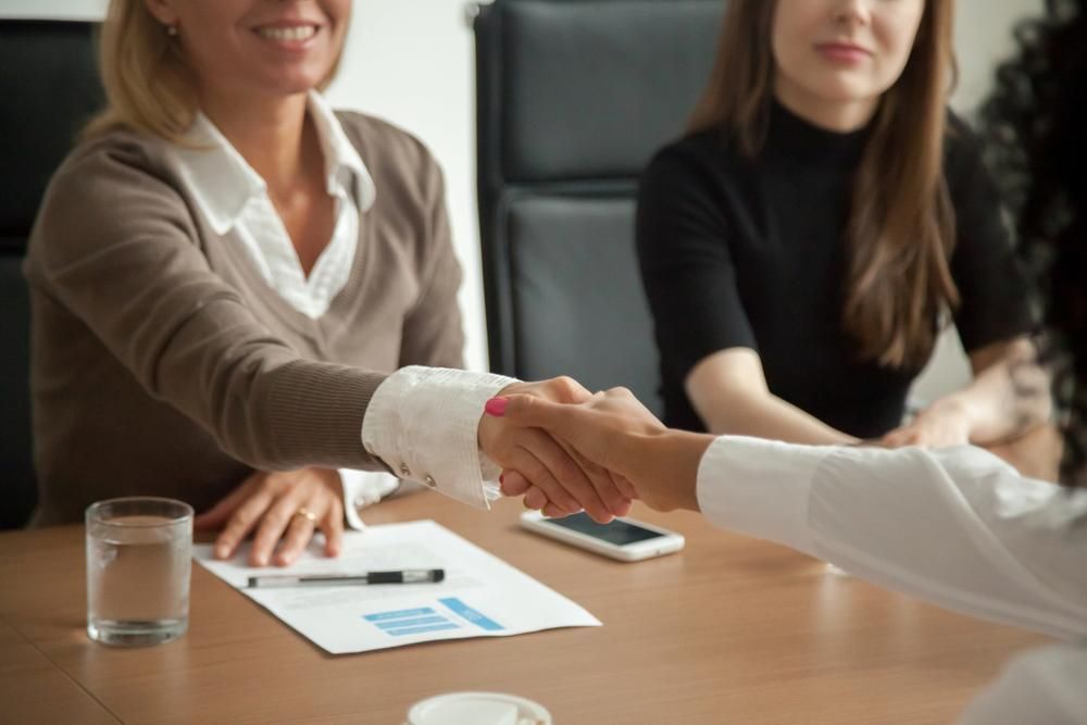 A Woman is Shaking Hands With Another Woman at a Table — Median Law In Bundaberg Central, QLD
