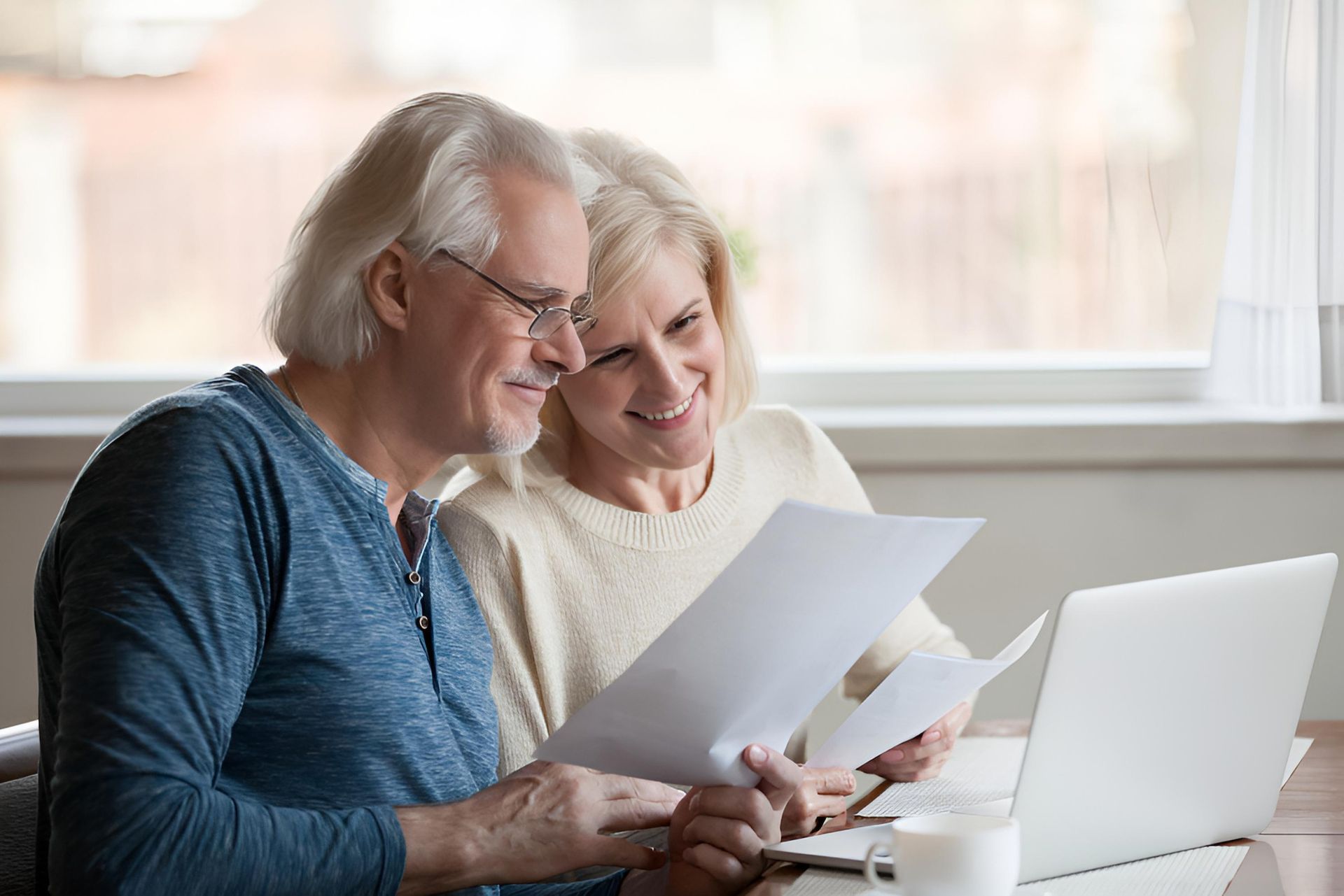 An Elderly Couple is Sitting at a Table Looking at Papers and a Laptop — Median Law In Mackay, QLD