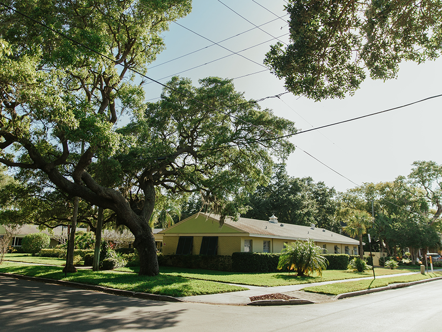 Yellow house with green lawn, corner lot, mature trees, power lines overhead.