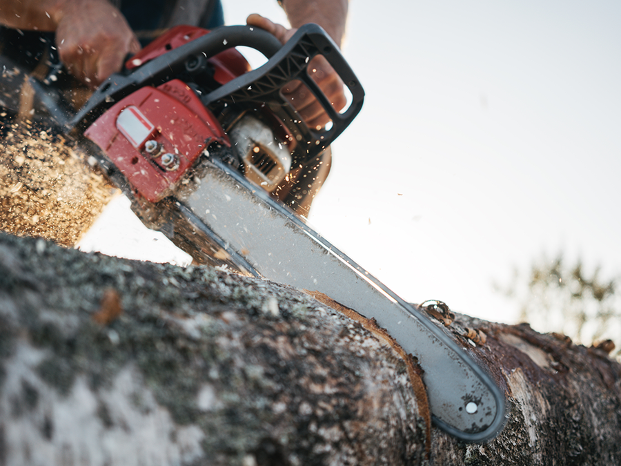 Person cutting wood with a red chainsaw; wood chips flying.