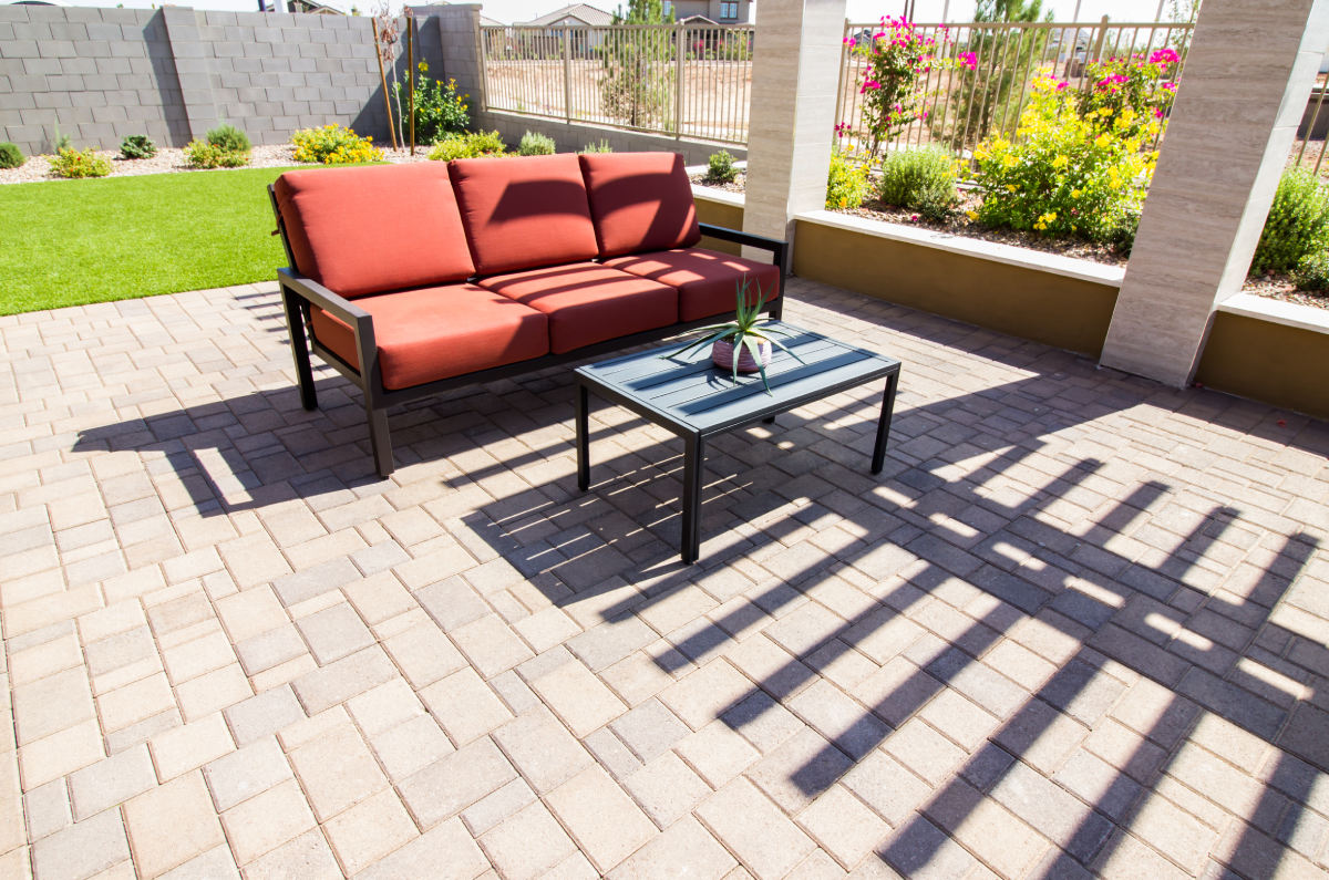Patio with brick pavers, red sofa, and small table under a pergola, sunny backyard.