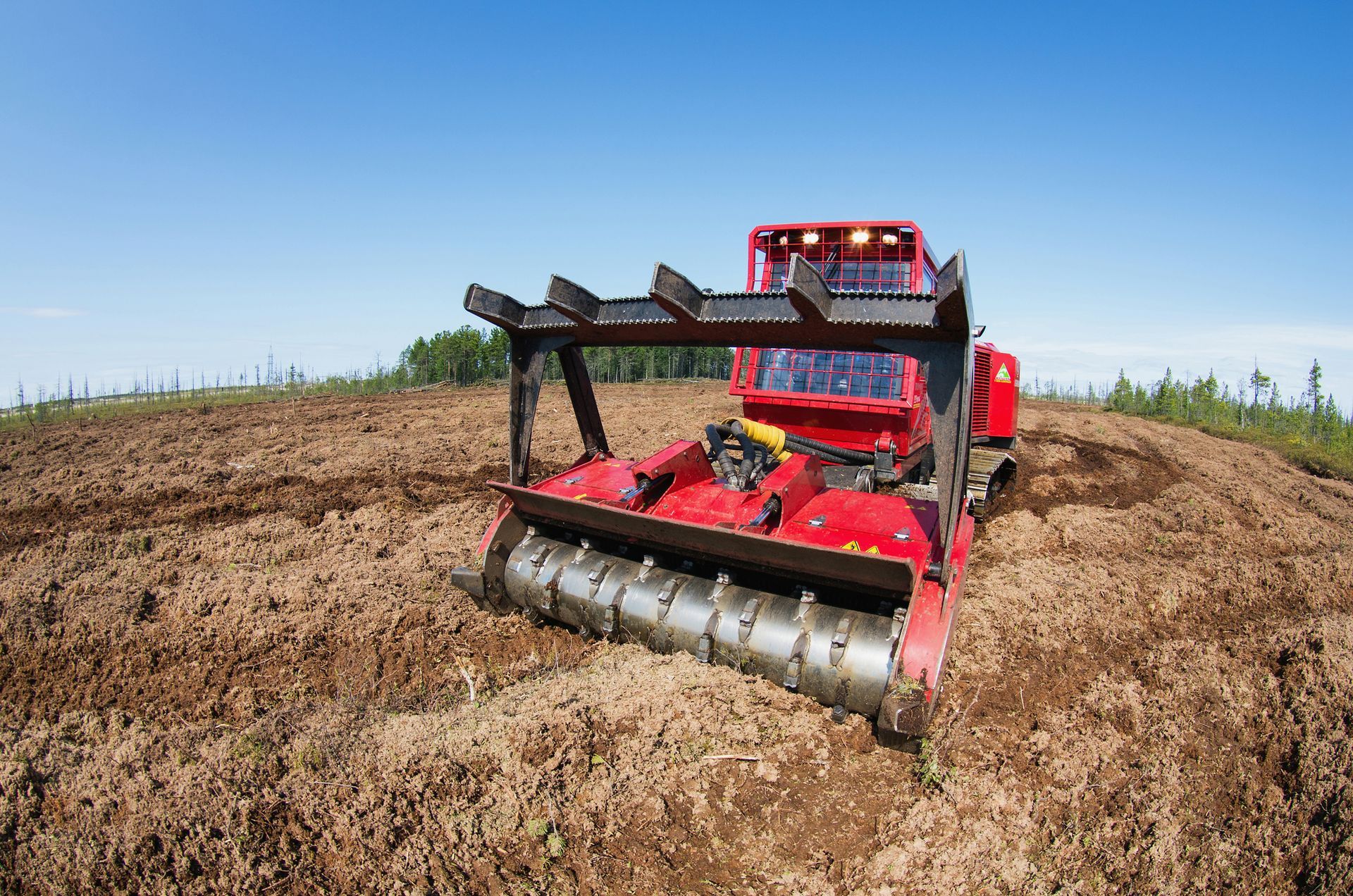 Red mulching machine on a brown field under a clear blue sky.