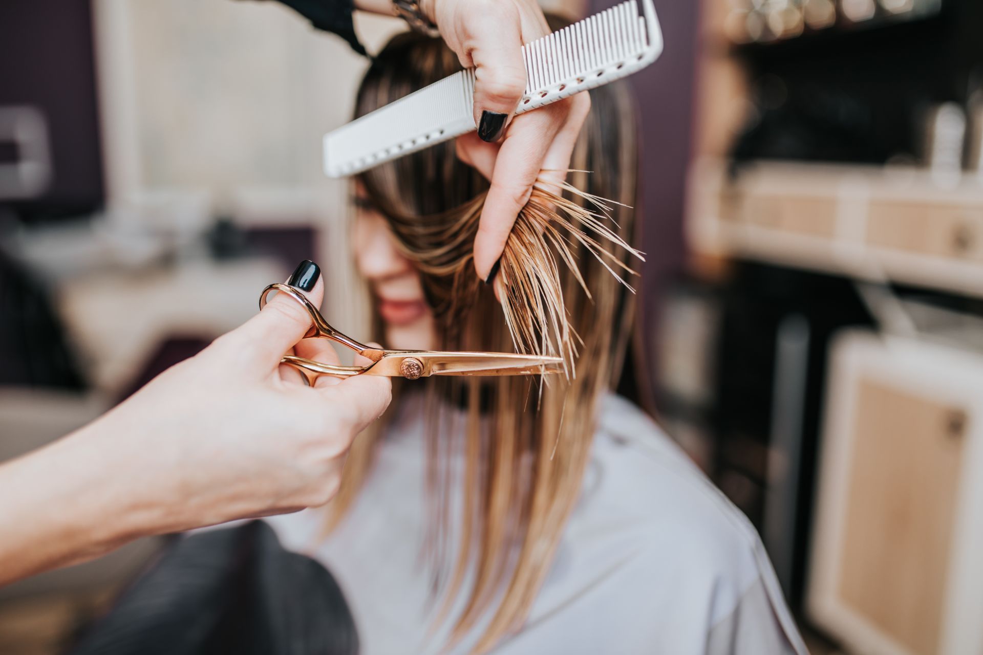 Hairdresser cutting a client's hair with scissors and comb in a salon.