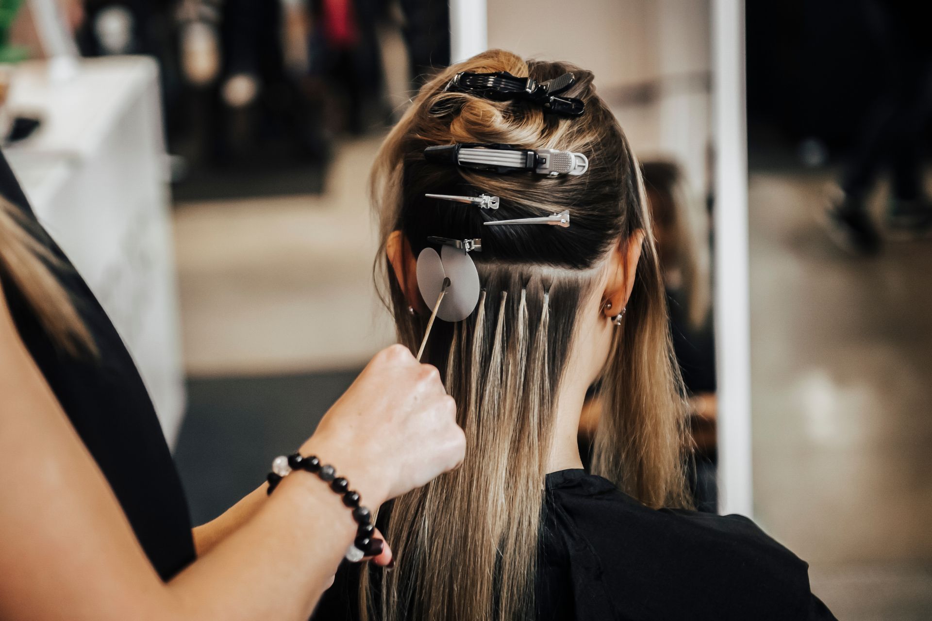 Hair extensions being applied at a salon. Blonde hair is clipped back, with new extensions attached.
