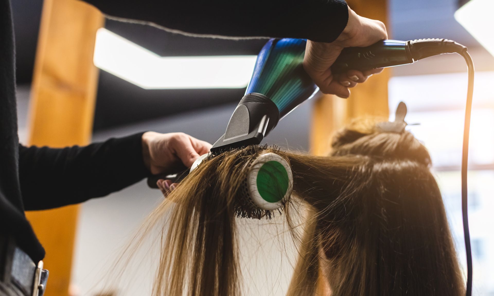 Hairdresser using a blow dryer and brush on a client's hair in a salon.