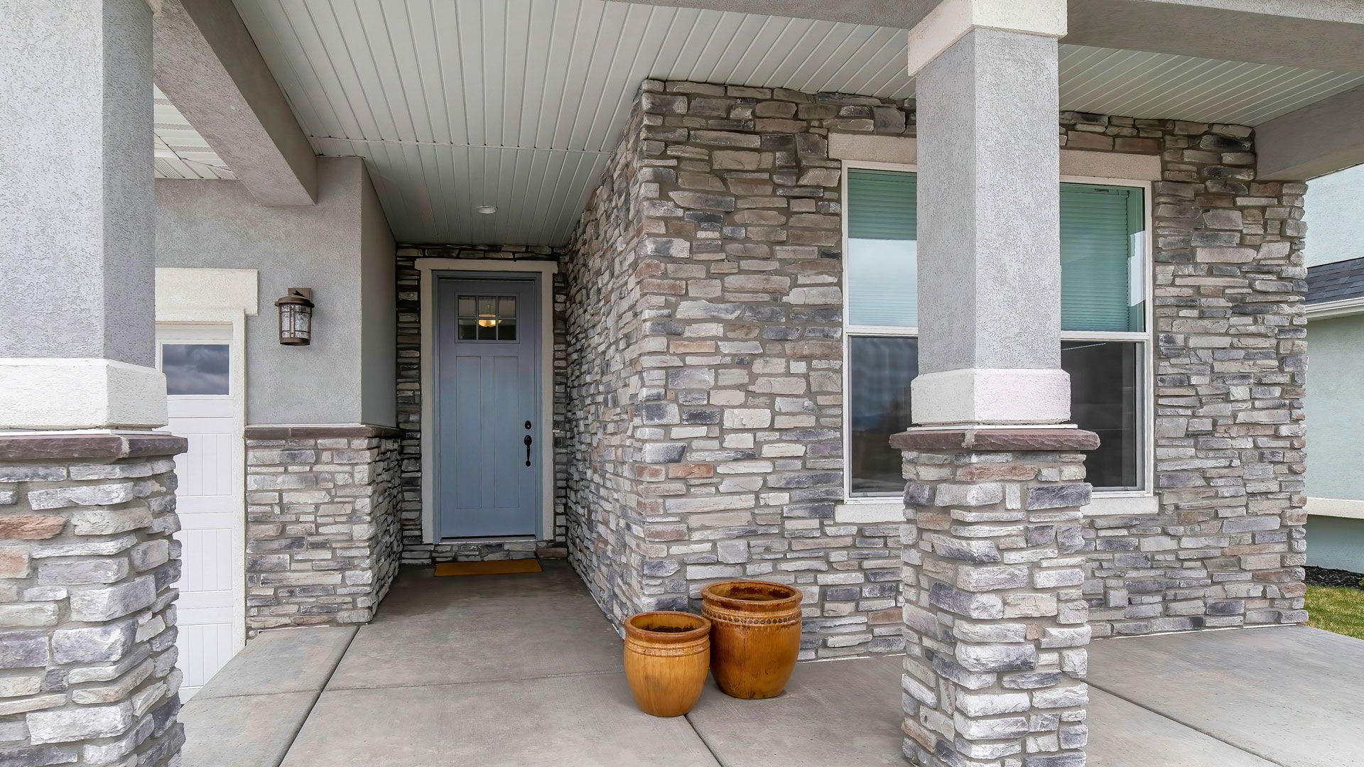 Covered entryway with stone facade and blue door, flanked by columns.