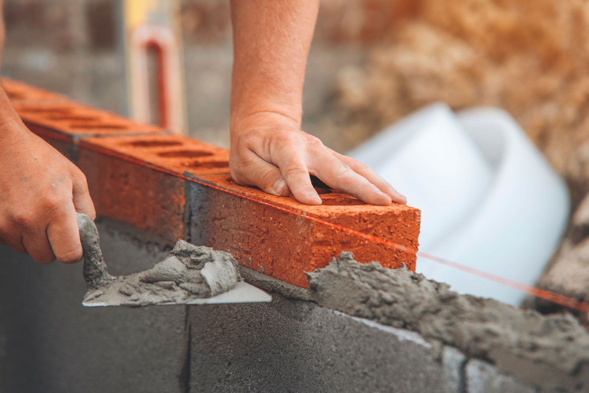 Bricklayer placing a brick onto mortar; close-up of hands and brick wall under construction.