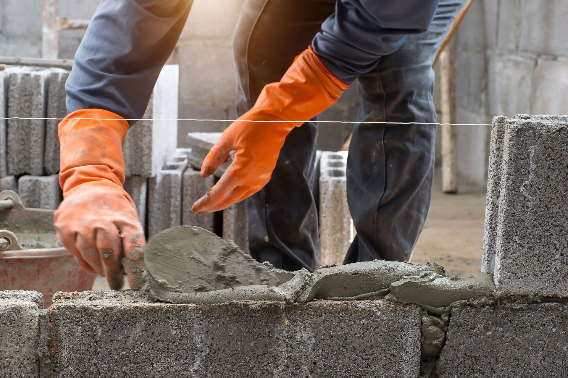 A construction worker in orange gloves spreading mortar on cinder blocks.