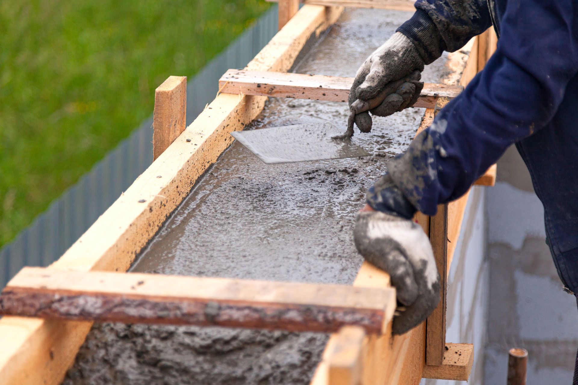 Person using a trowel to smooth wet concrete in a wooden form.