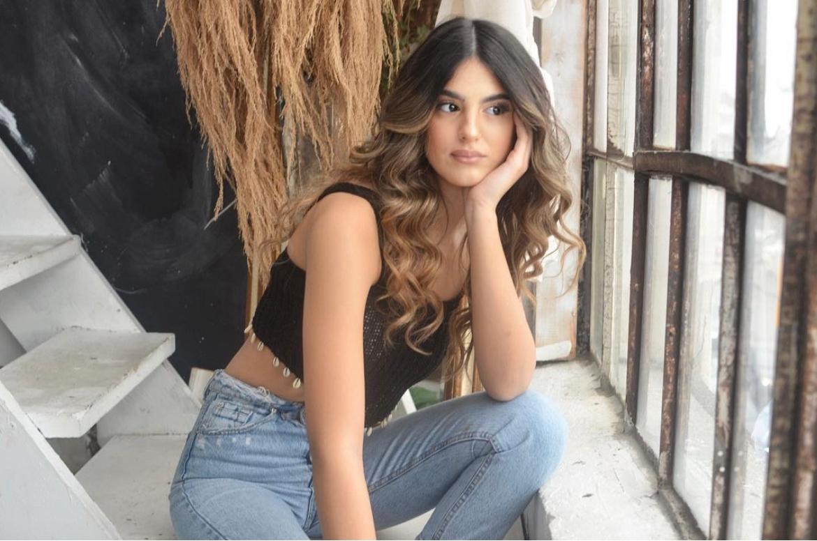 young woman wearing jeans with balayage curly hair sitting next to window