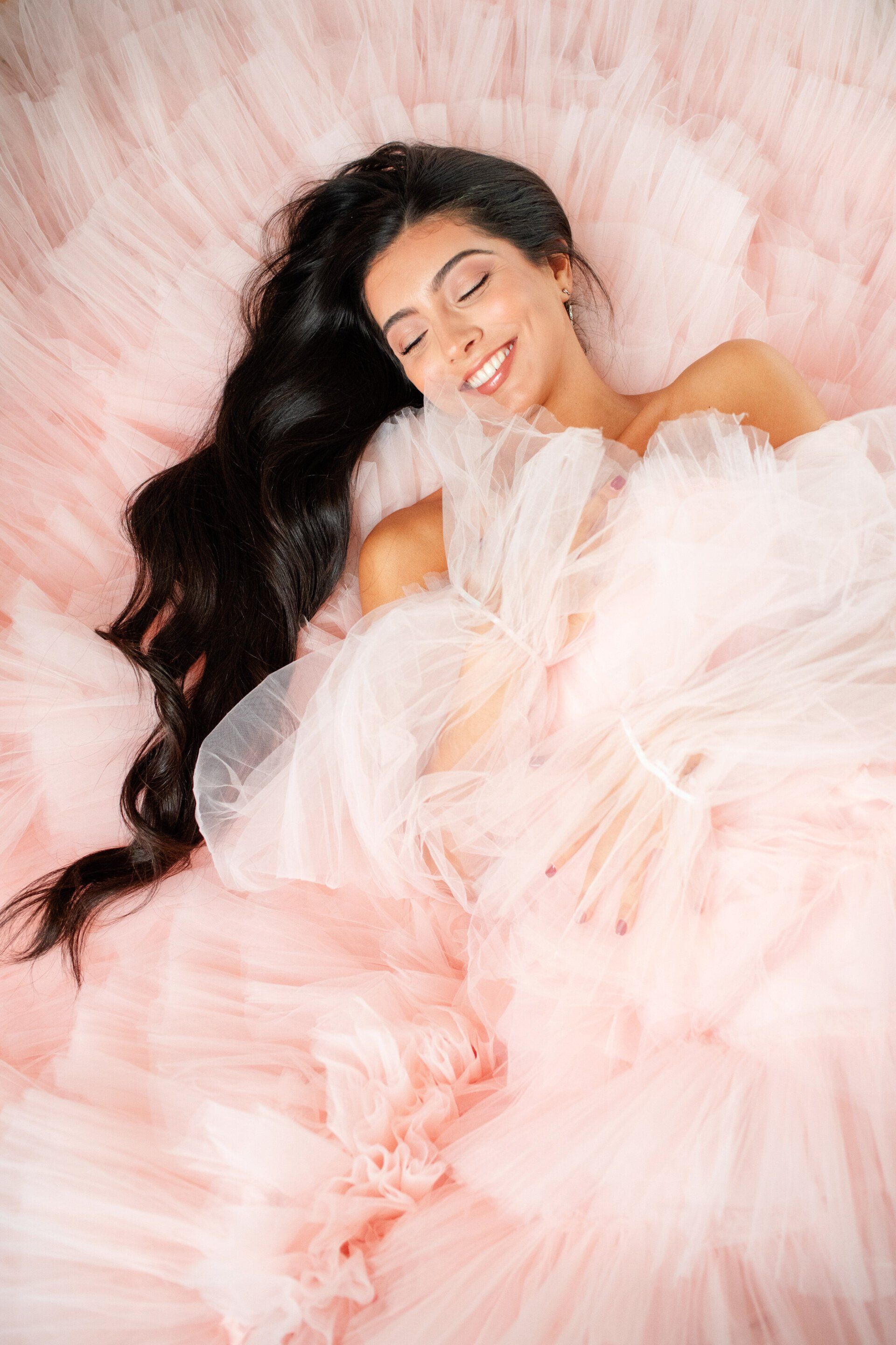A woman in a pink tule dress is laying on a bed with her eyes closed.