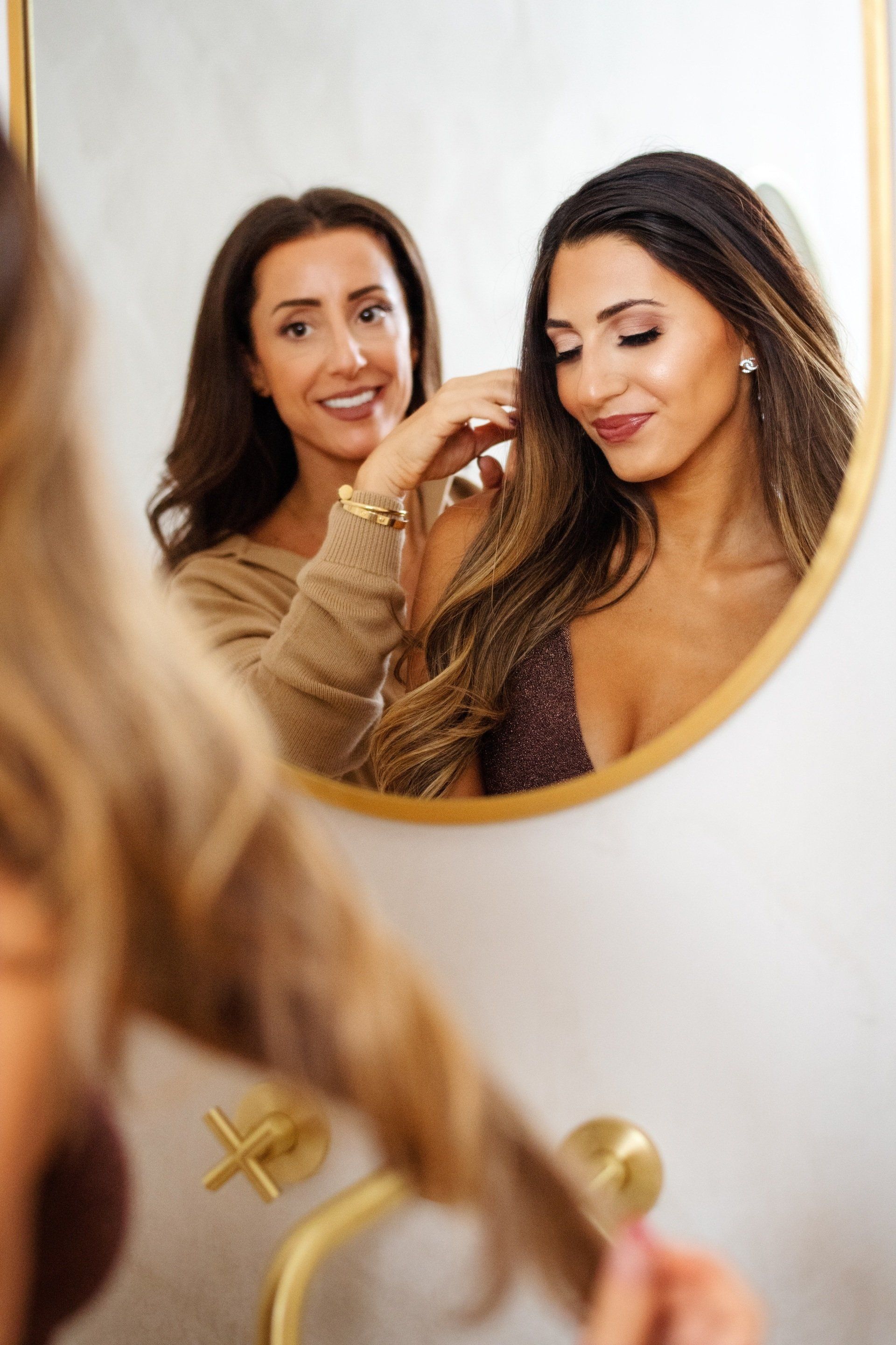 Two women are looking at their reflection in a mirror.