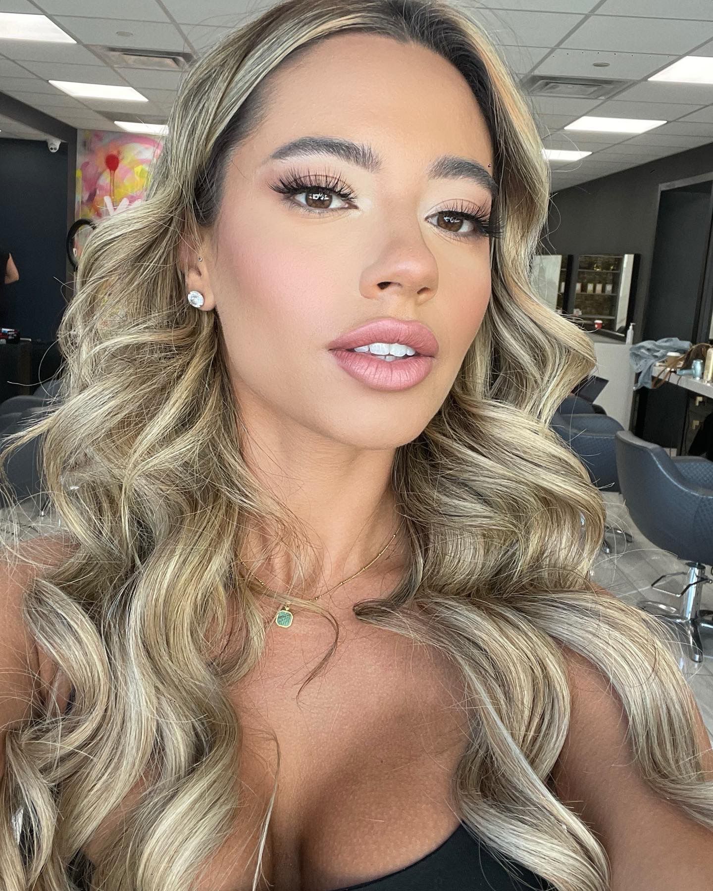 A woman with long blonde hair is taking a selfie in a salon.