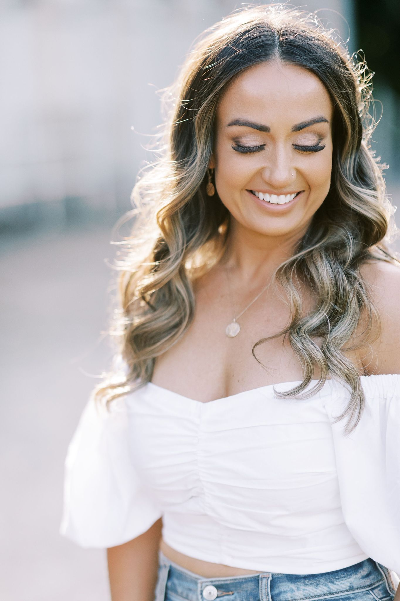 A woman wearing a white off the shoulder top and jeans is smiling.
