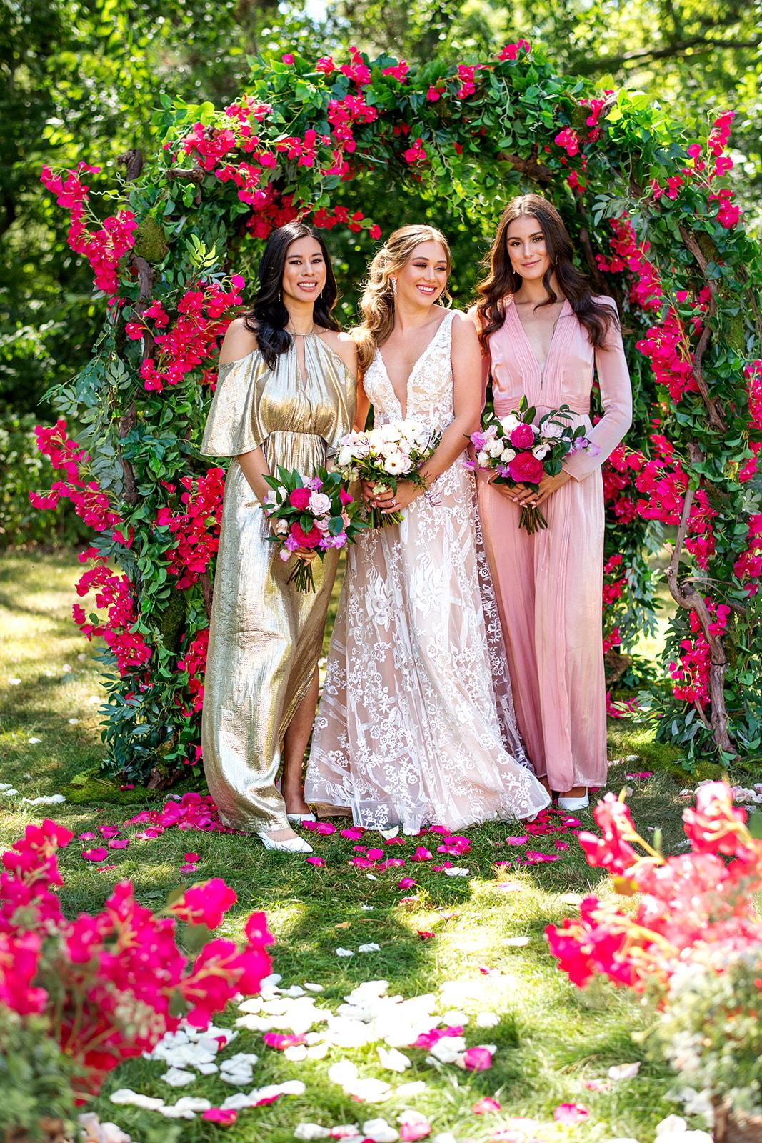 A bride and her bridesmaids are posing for a picture in front of a rose arch.