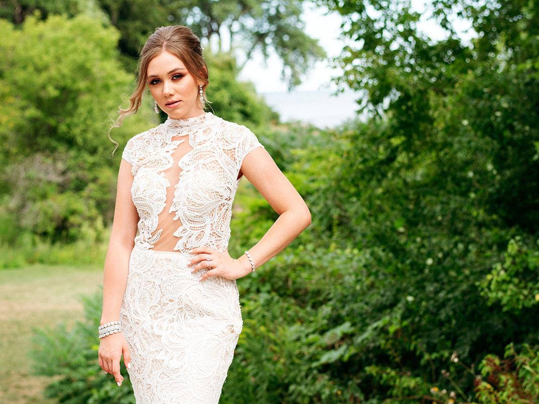 A woman in a white lace dress is standing in a park.