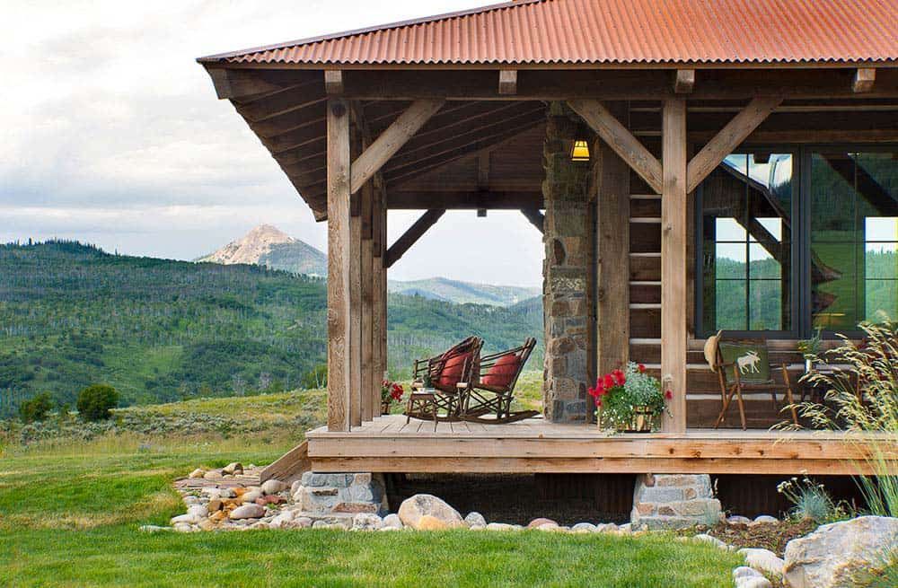 Two rocking chairs are sitting on a porch of a house with mountains in the background.