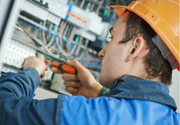 A man wearing a hard hat is working on an electrical box. A man wearing a hard hat is working on an electrical box.