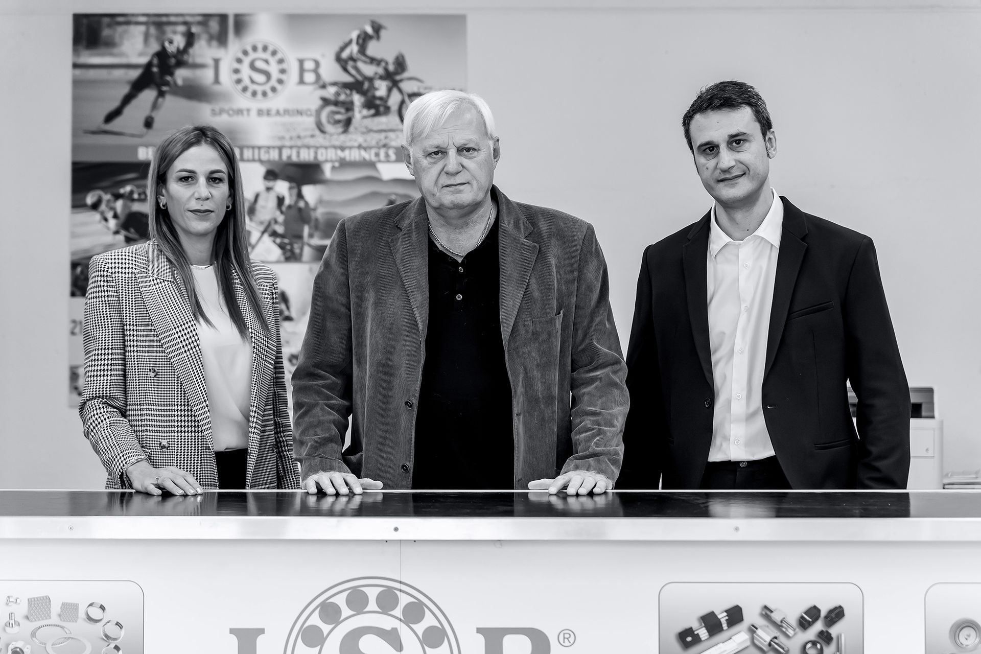 Tre persone in piedi dietro un bancone con il logo ISR: due uomini e una donna.