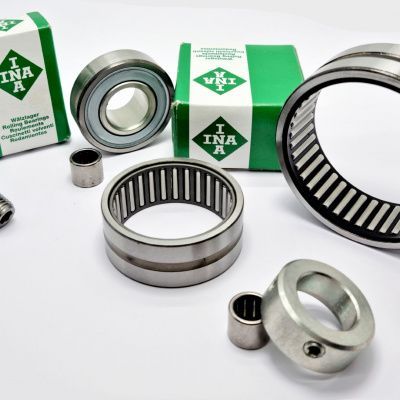 Primo piano di diversi cuscinetti a marchio INA e relativi componenti, di varie dimensioni, su una superficie bianca. Sono visibili anche i riquadri verdi.