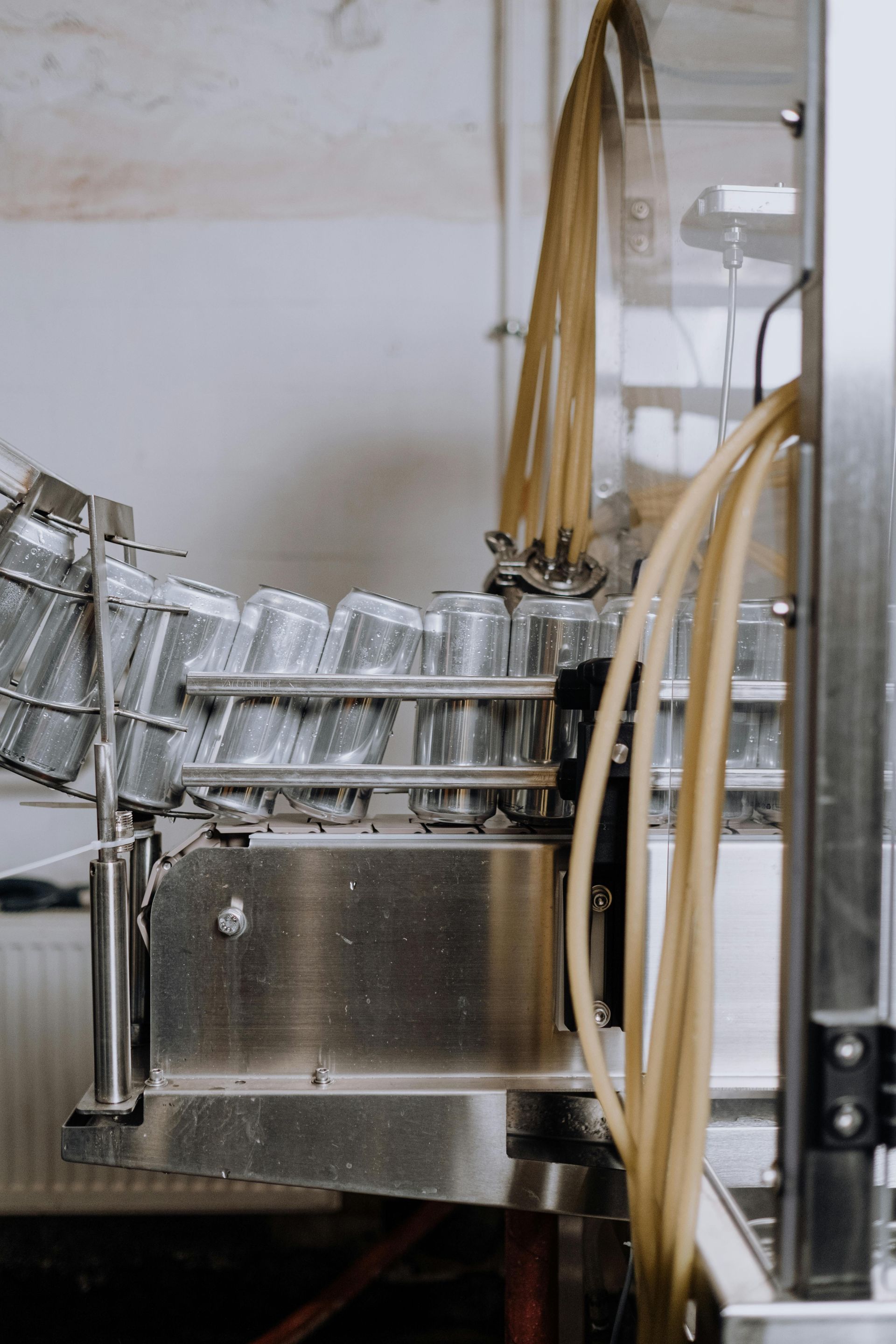 Lattine di alluminio in movimento lungo una linea di produzione industriale, con tubi e macchinari visibili.