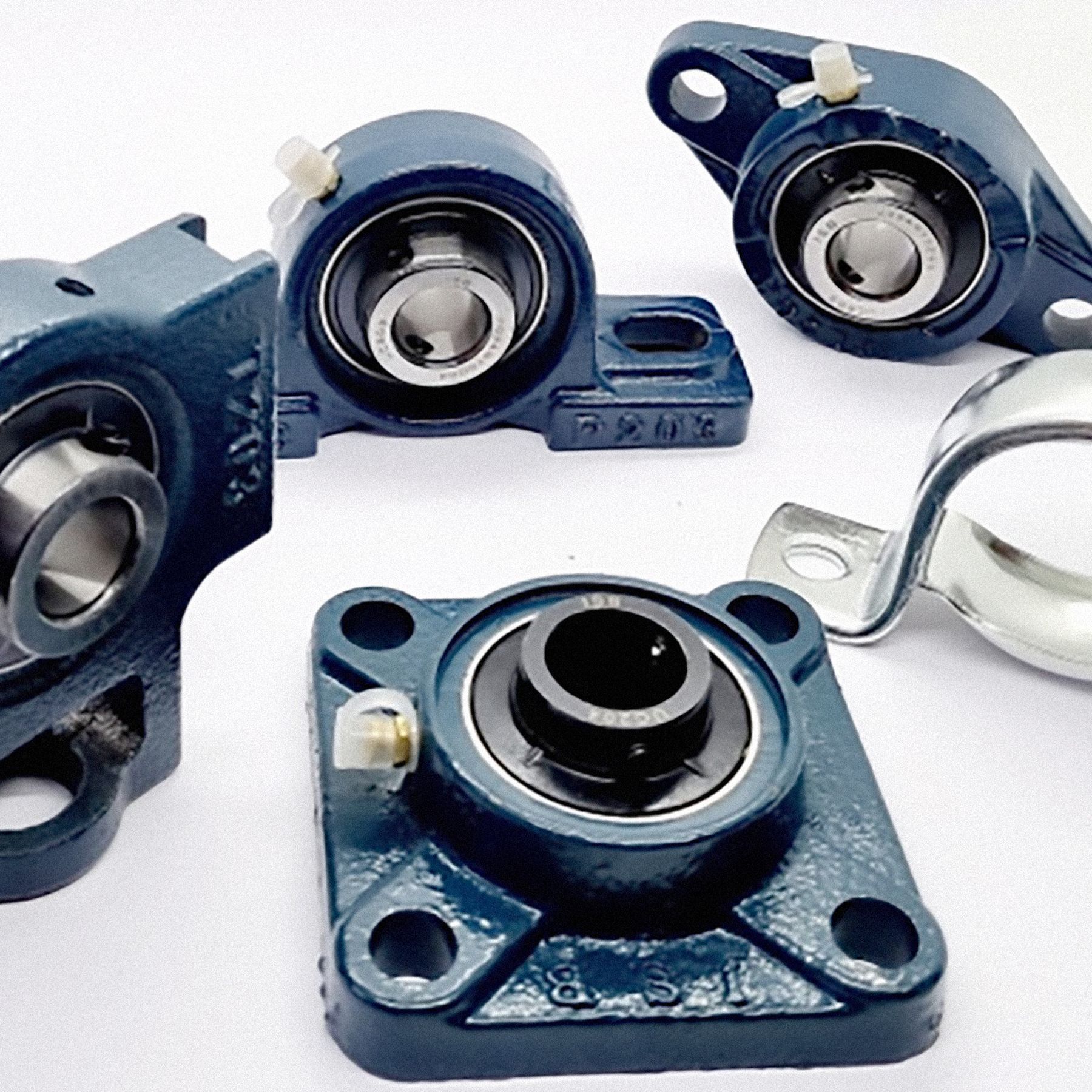 Cuscinetti a cuscinetto industriali blu, di varie forme e supporti, su una superficie bianca.