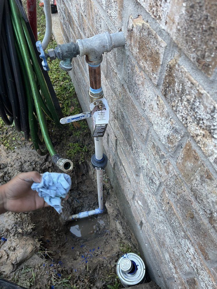 A person is cleaning a faucet outside of a brick wall.