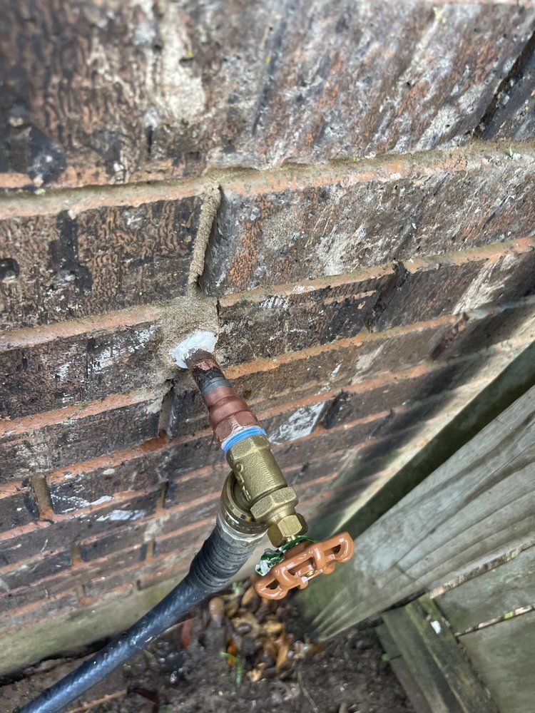A hose is attached to a brick wall next to a wooden fence.