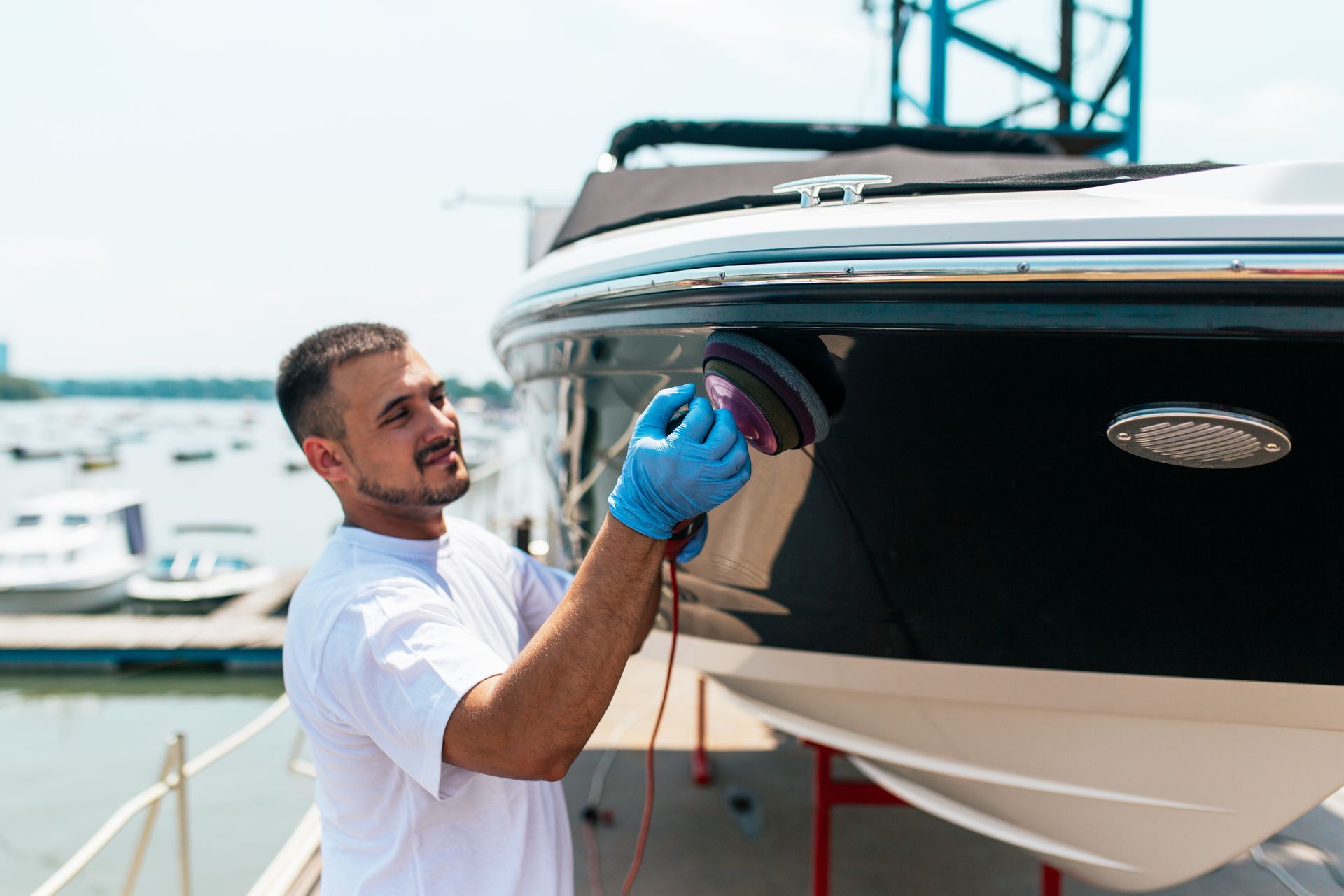 Man polishing a yacht hull with a blue cloth at a marina