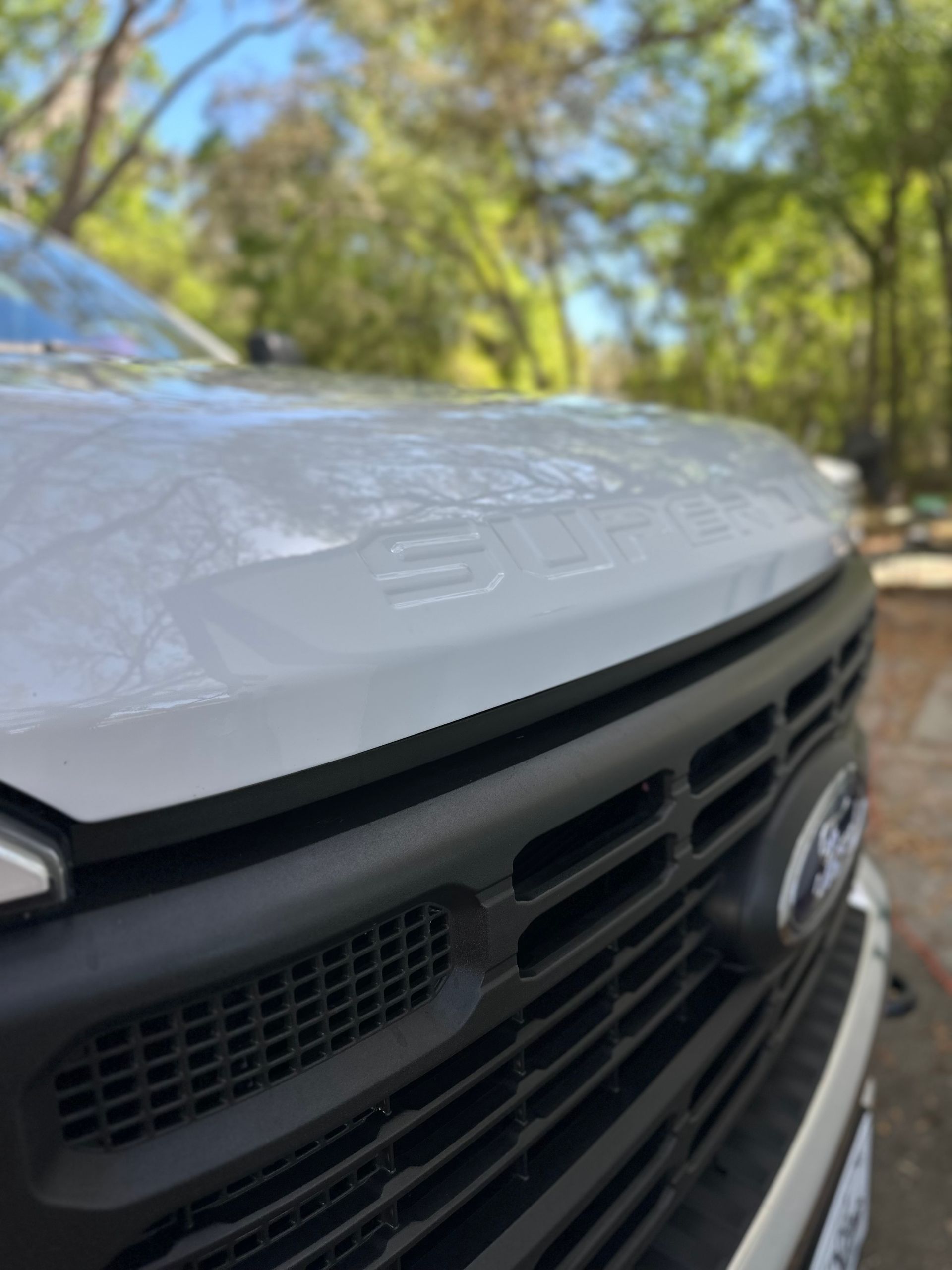 White SUV in auto repair shop while mechanic works on a raised dark car in the background