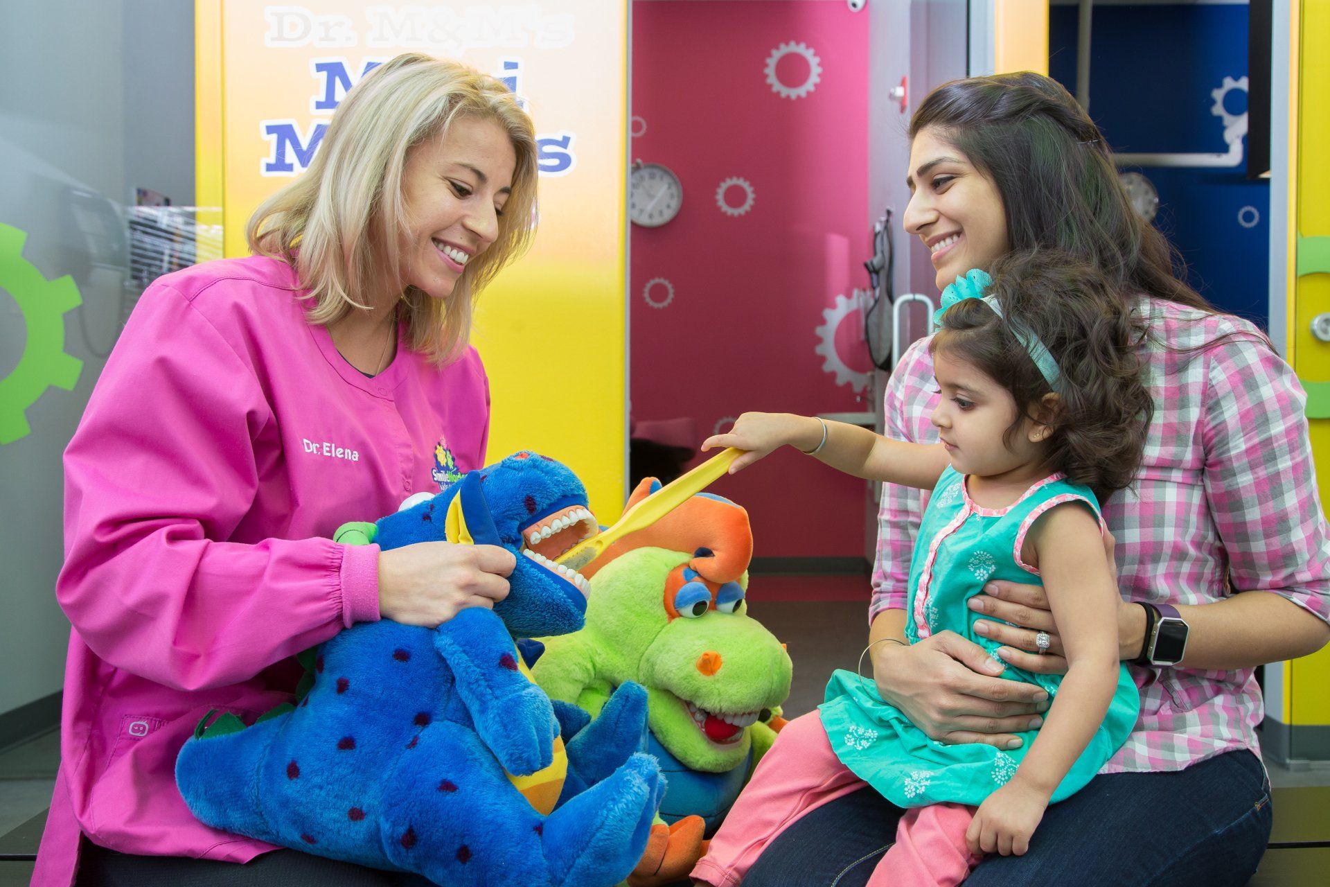A woman is brushing a child 's teeth with a toothbrush while holding a stuffed animal.