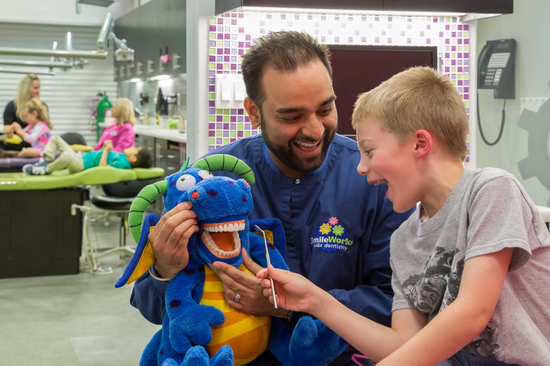 A dentist is teaching a young boy how to brush his teeth with a stuffed animal.