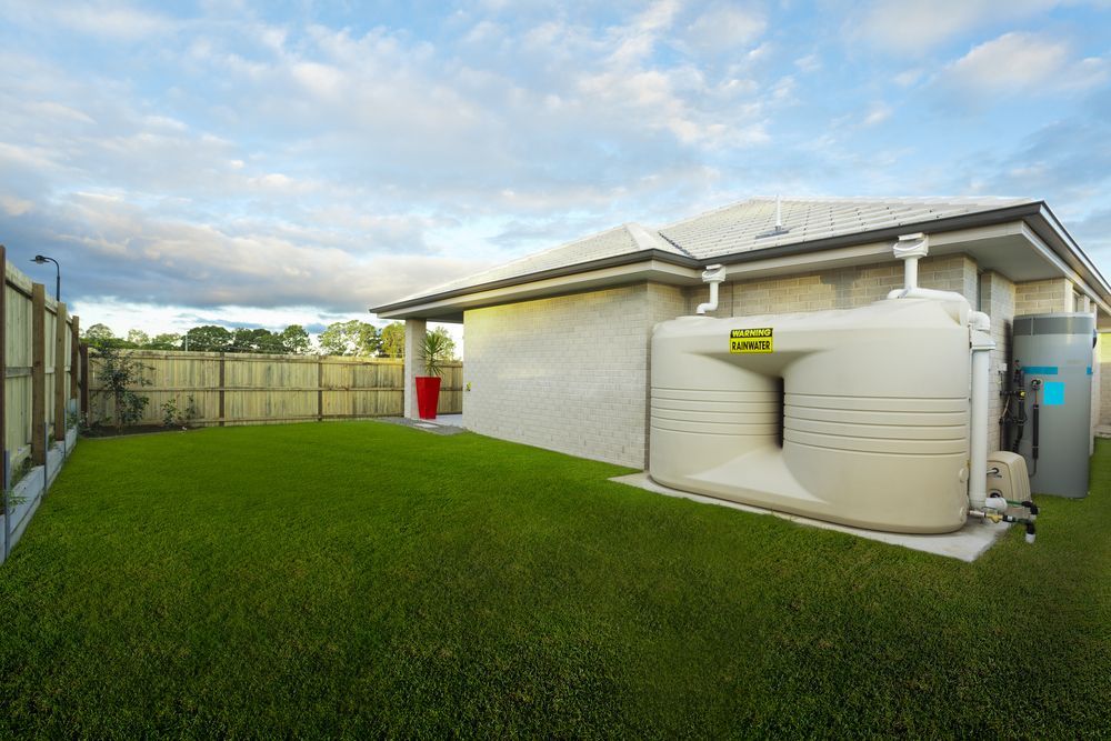 A Large White Tank Is Sitting In The Backyard Of A House — Clear and Clean Water Tank Cleaning Services in Newcastle, NSW