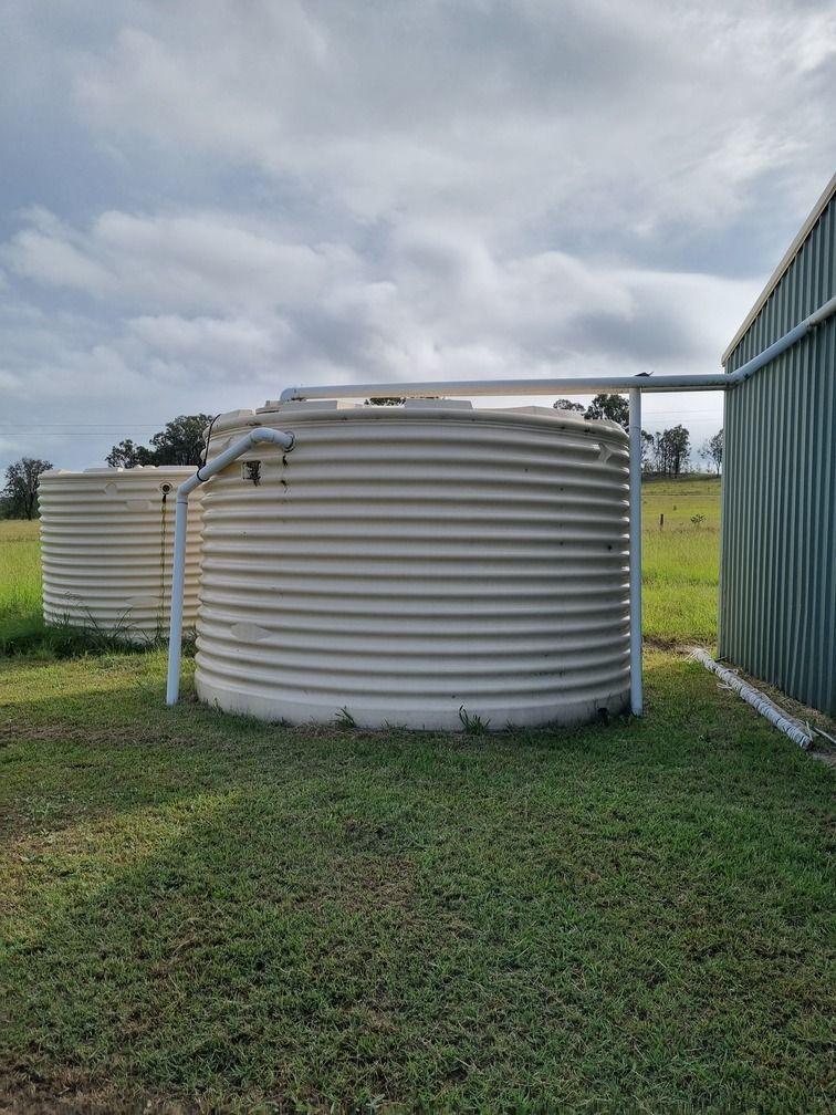 A Green Water Tank Is Sitting On Top Of A Wooden Platform In The Middle Of A Forest — Clear and Clean Water Tank Cleaning Services in Bridgman, NSW