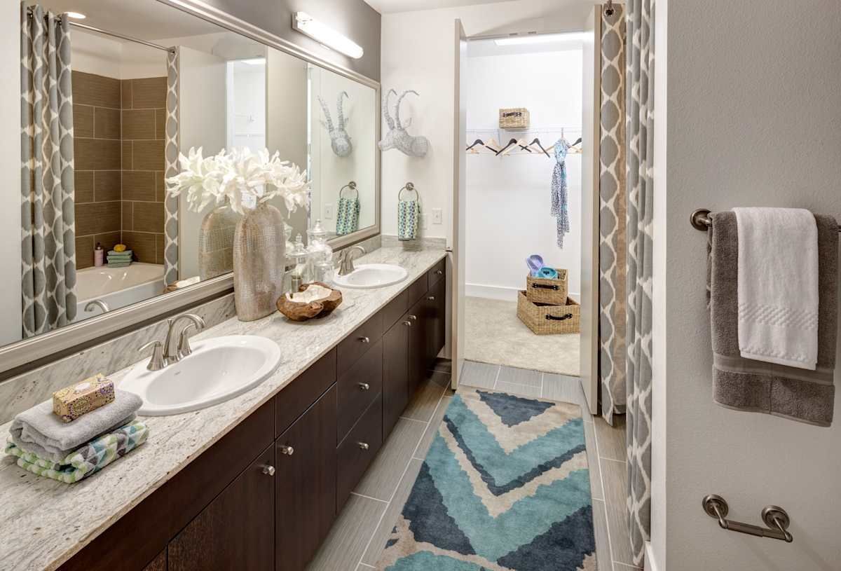 A bathroom with two sinks , two mirrors , a rug and a walk in closet.