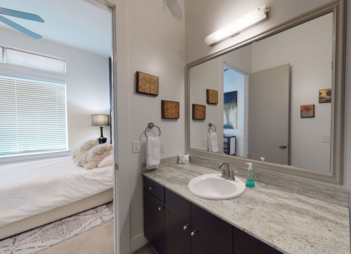 A bathroom with a sink and a large mirror next to a bedroom.