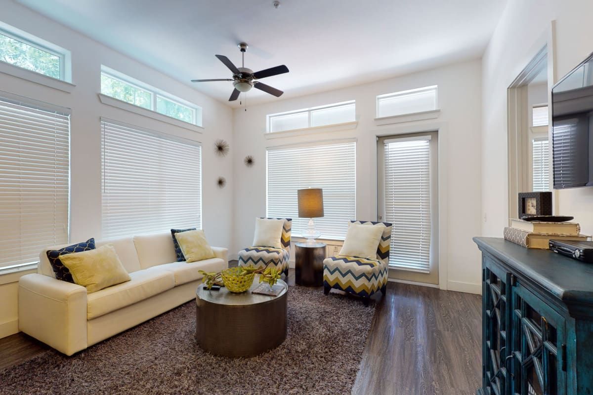 A living room with a couch , two chairs , a coffee table and a ceiling fan.