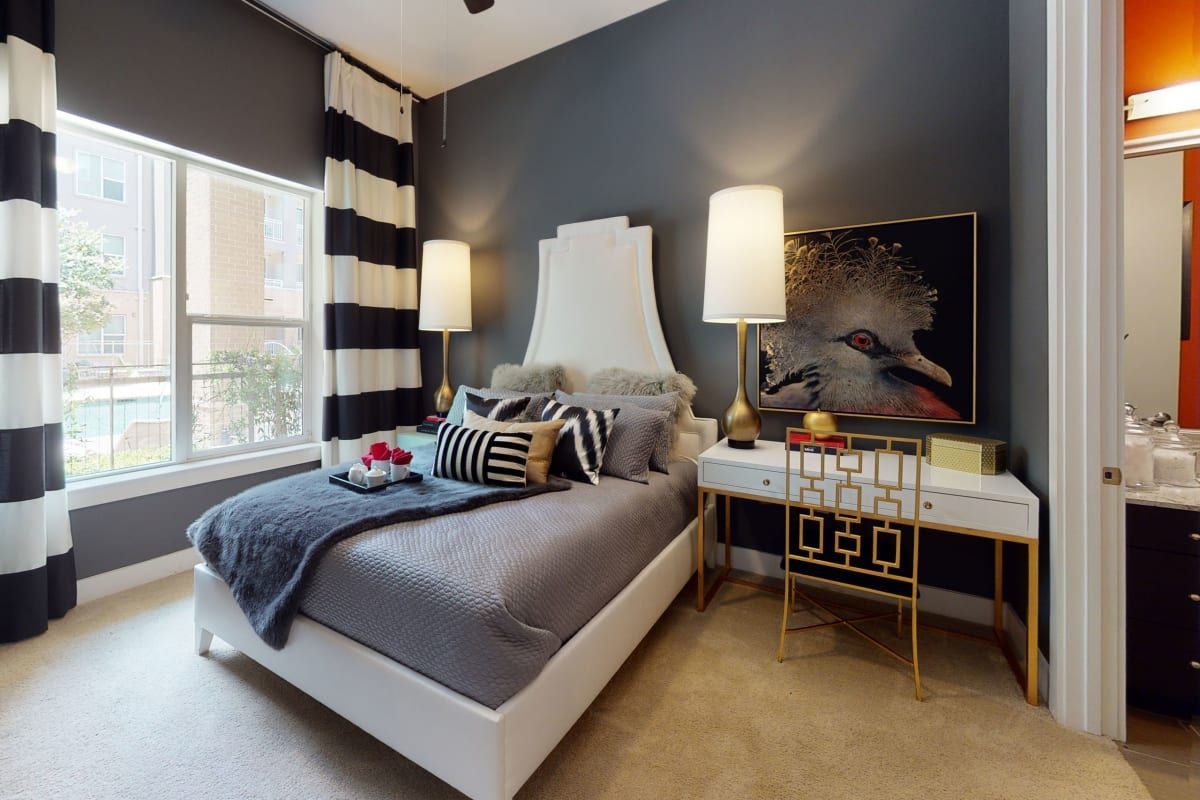 A bedroom with a bed , desk , lamps and a window.