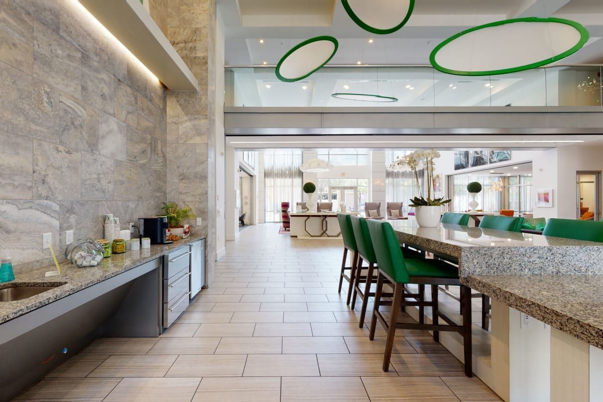 There are many green chairs and ottomans in the lobby of a hotel.