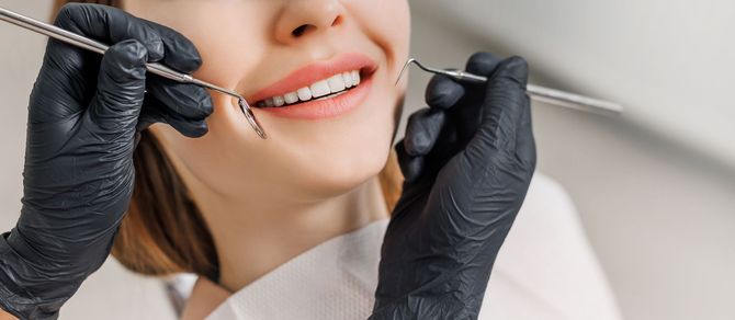 Dentist examining a smiling patient’s teeth with dental tools in a clinic