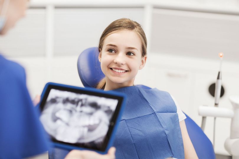 Dentist and nurse wearing masks treat a smiling patient in a bright dental clinic