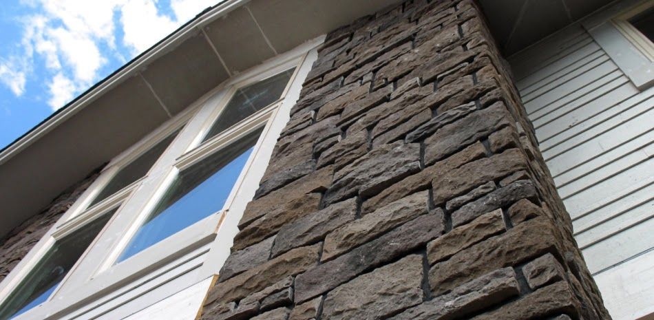Stone facade on building with white window frames and siding, blue sky in background.