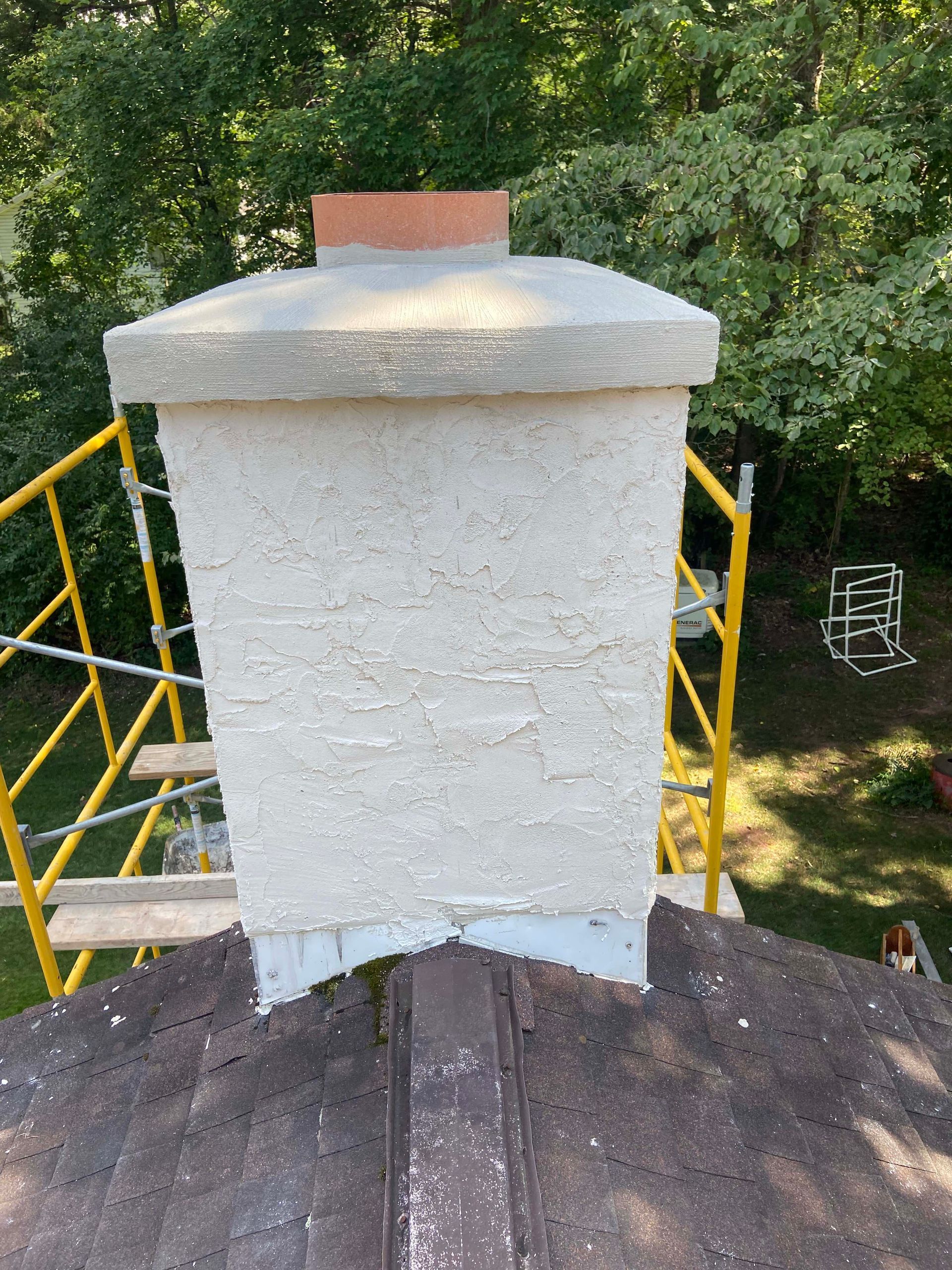 Brick chimney on a tiled roof against a blue sky.