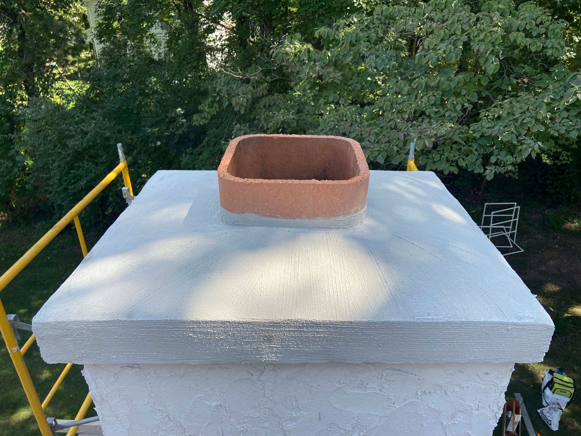 Brick chimney against a blue sky, on a gray shingle roof.
