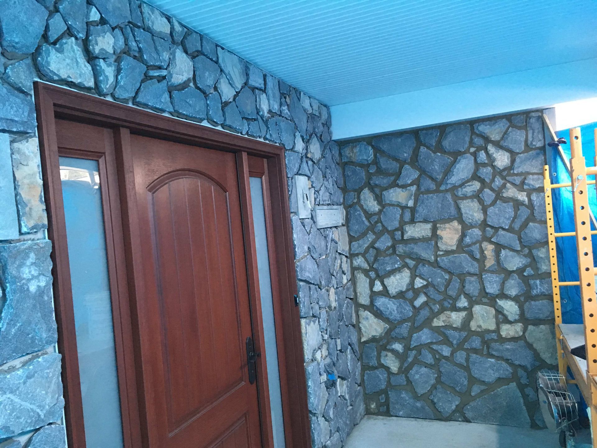 Stone wall composed of horizontal rectangular pieces in shades of gray, gold, and rust.