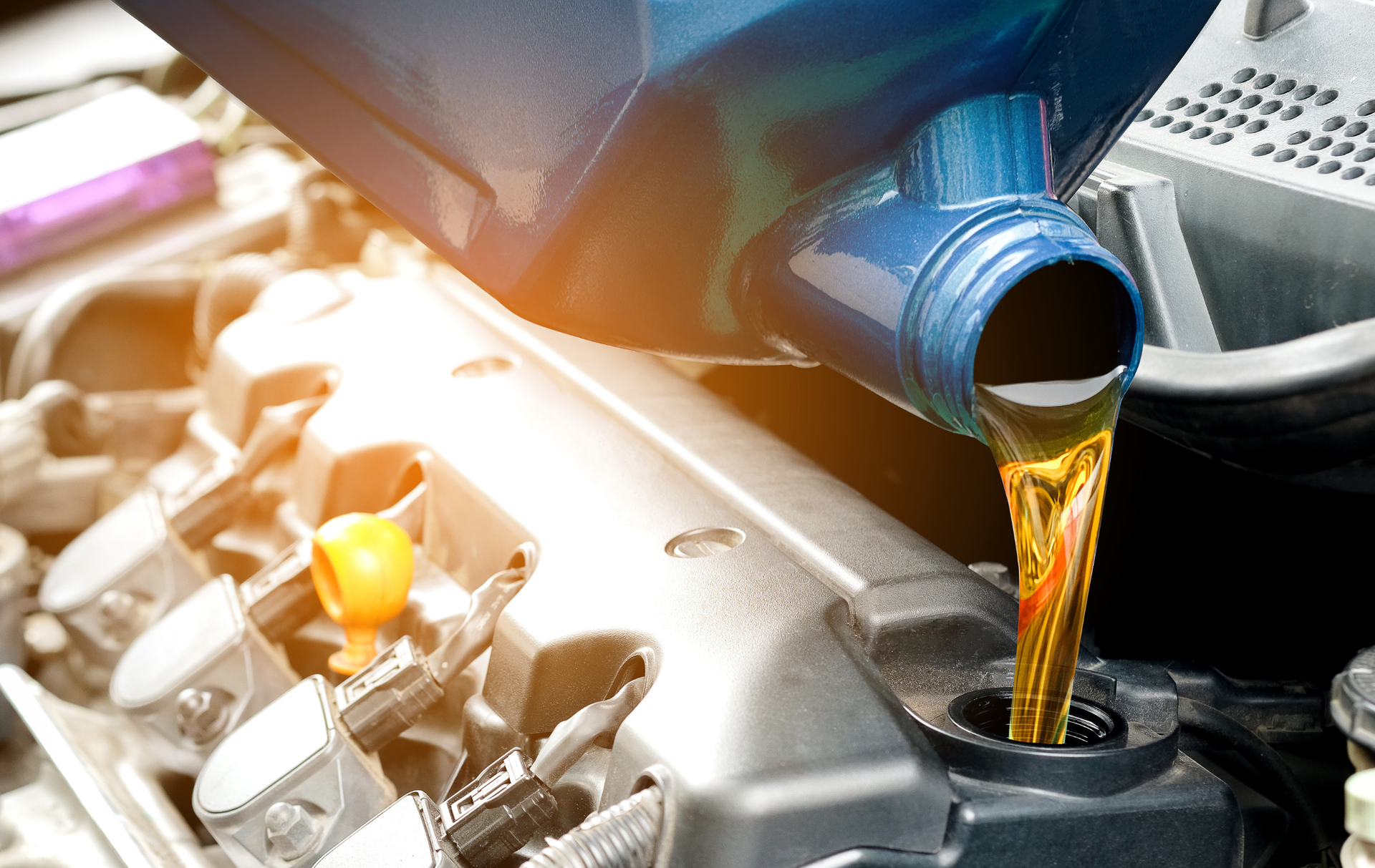 A close up of a person pouring oil into a car engine.