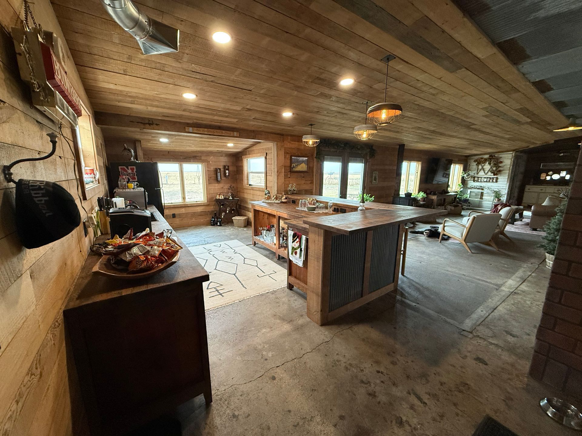 Interior of a large wooden barn with vaulted ceiling, wood floor, and lights. Bar and pool table visible.
